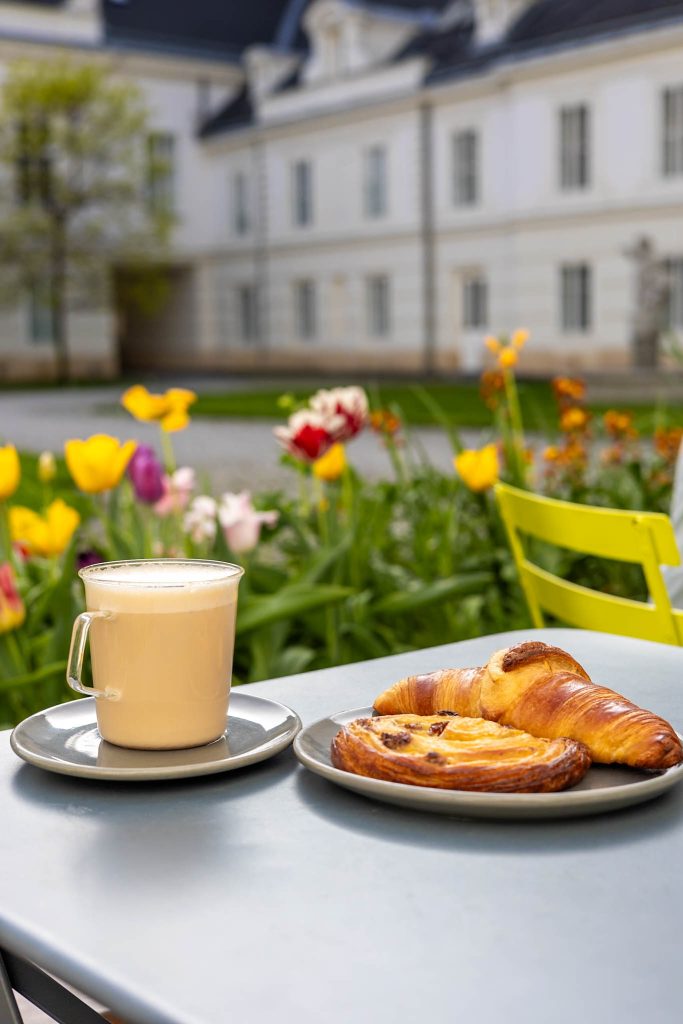 Chai Latte und Croissant auf einem Teller im Cafe Carl Ludwig in Wien, im Hintergrund bunte Tulpen.