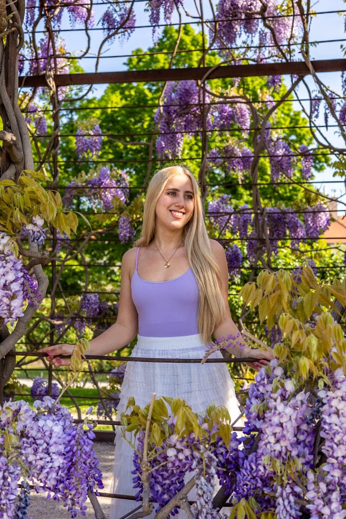 Blonde Frau inmitten von lila blühendem Wisteria im Schönbrunn Schlosspark in Wien.