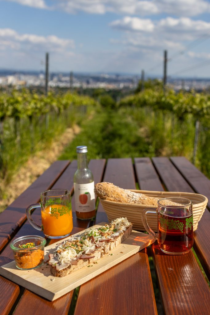 Schinkenbrot, Litauer und Wecker und Getränke auf einem Tisch bei einem Heurigen am Nussberg in Wien.