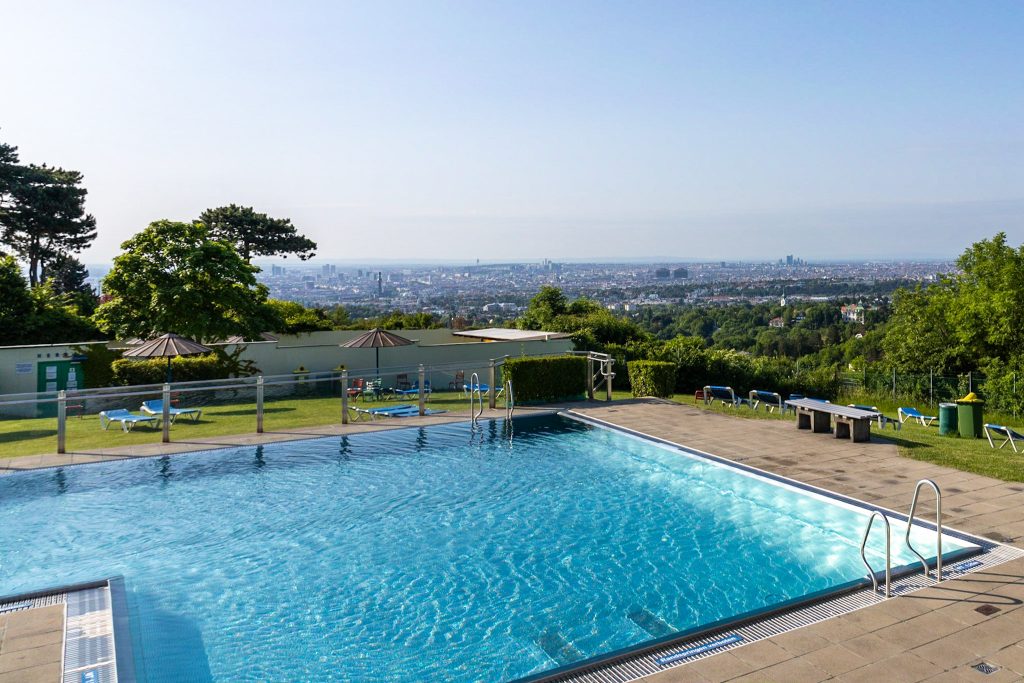 Pool im Krapfenwaldbad in Wien mit Blick auf die Stadt.