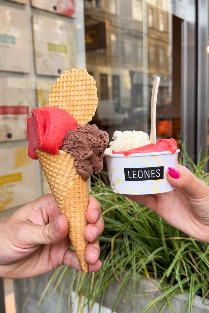 Eine Tüte Eis mit zwei Kugeln und Waffel und ein Becher Eis mit Löffel und 2 Sorten von Leones in Wien.